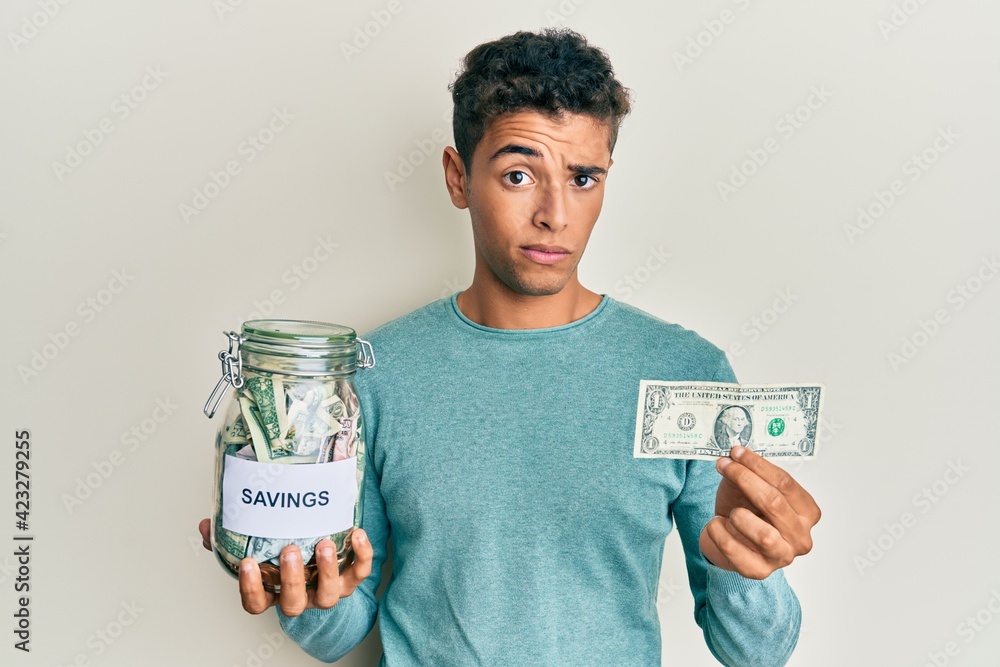 Young handsome african american man holding jar with savings skeptic and nervous, frowning upset because of problem. negative person. Young handsome african american man holding jar with savings skeptic and nervous, frowning upset because of problem. negative person.