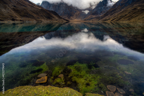 A polarizing filter shows rocks and green grass in Lake Carhuacocha during a reflection and sunrise in the Cordillera Huayhuash of the Andes Mountains in Peru.      photo