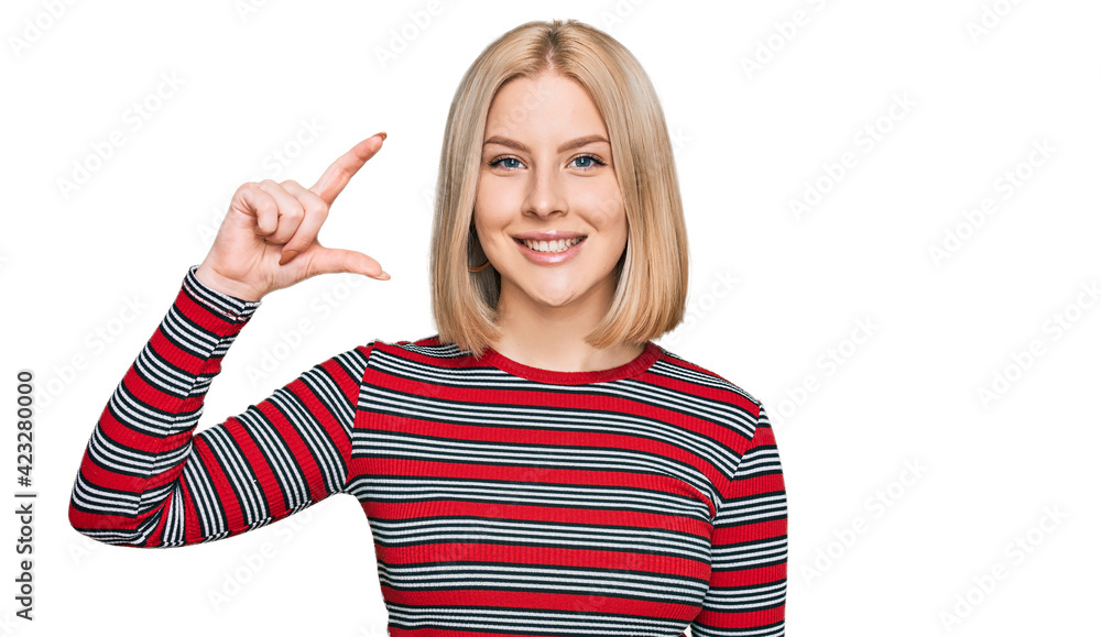 Young blonde woman wearing casual clothes smiling and confident gesturing with hand doing small size sign with fingers looking and the camera. measure concept. Young blonde woman wearing casual clothes smiling and confident gesturing with hand doing small size sign with fingers looking and the camera. measure concept.