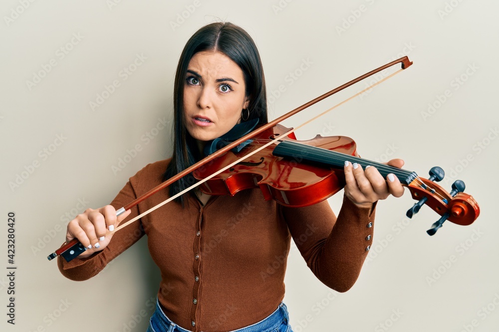 Young brunette woman playing violin clueless and confused expression. doubt concept. Young brunette woman playing violin clueless and confused expression. doubt concept.