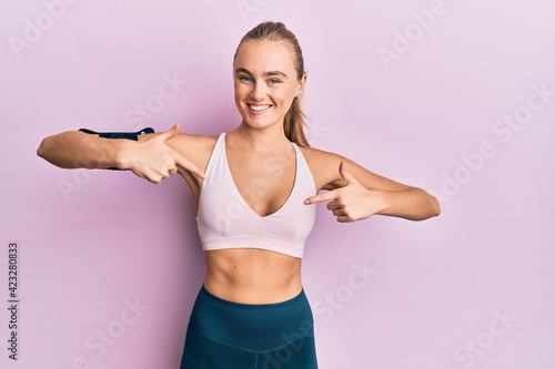 Beautiful blonde woman wearing sportswear and arm band looking confident with smile on face  pointing oneself with fingers proud and happy.