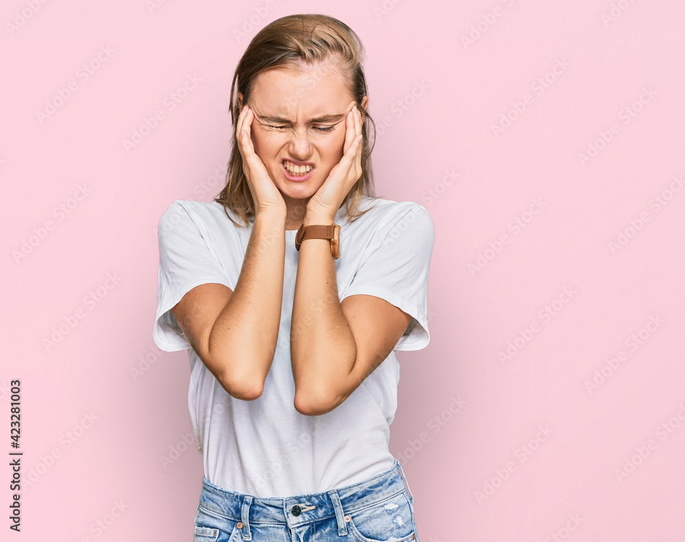 Beautiful young blonde woman wearing casual white t shirt with hand on head, headache because stress. suffering migraine. Beautiful young blonde woman wearing casual white t shirt with hand on head, headache because stress. suffering migraine.