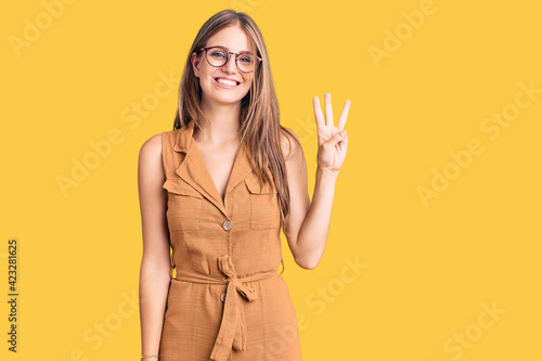 Young beautiful blonde woman wearing casual clothes and glasses showing and pointing up with fingers number three while smiling confident and happy. © Krakenimages.com