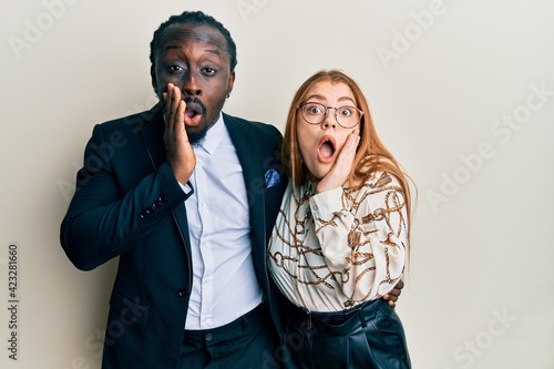 Young interracial couple wearing business and elegant clothes afraid and shocked, surprise and amazed expression with hands on face