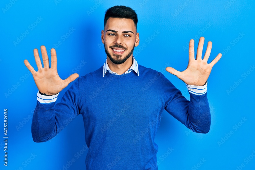 Young hispanic man with beard wearing casual blue sweater showing and pointing up with fingers number ten while smiling confident and happy. Young hispanic man with beard wearing casual blue sweater showing and pointing up with fingers number ten while smiling confident and happy.