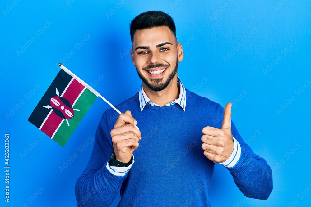 Young hispanic man with beard holding kenya flag smiling happy and positive, thumb up doing excellent and approval sign Young hispanic man with beard holding kenya flag smiling happy and positive, thumb up doing excellent and approval sign