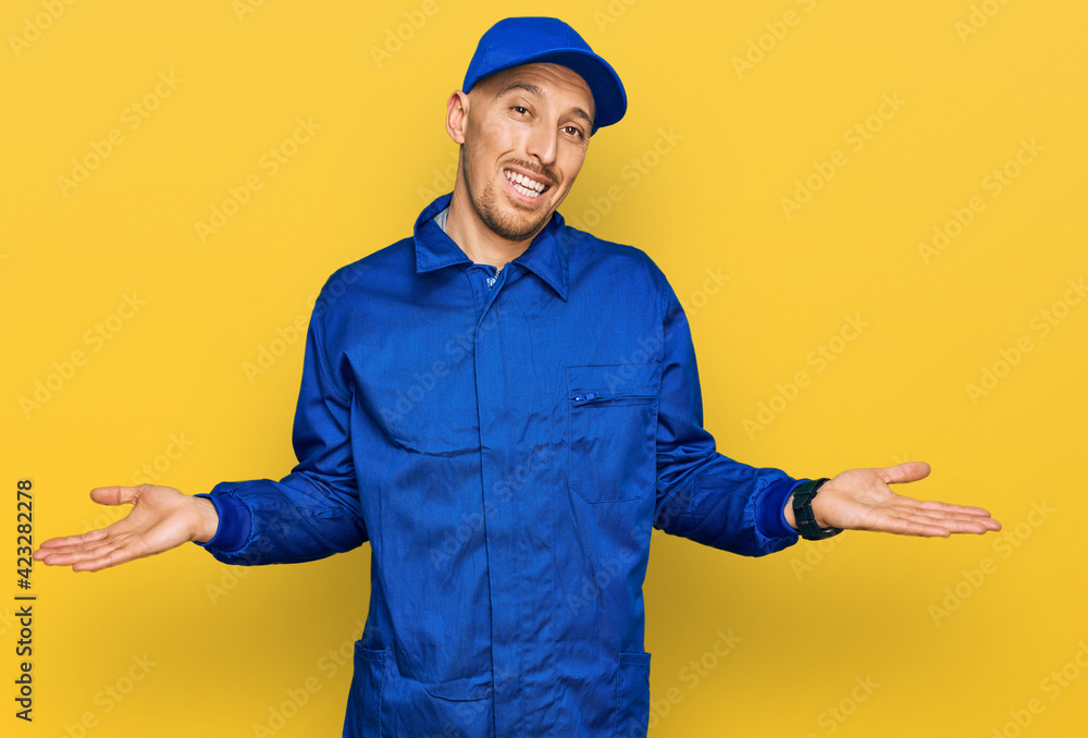 Bald man with beard wearing builder jumpsuit uniform smiling showing both hands open palms, presenting and advertising comparison and balance Bald man with beard wearing builder jumpsuit uniform smiling showing both hands open palms, presenting and advertising comparison and balance