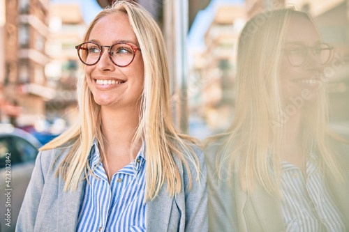 Young blonde businesswoman smiling happy leaning on the wall at the city.