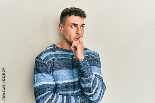 Hispanic young man wearing casual winter sweater thinking concentrated about doubt with finger on chin and looking up wondering