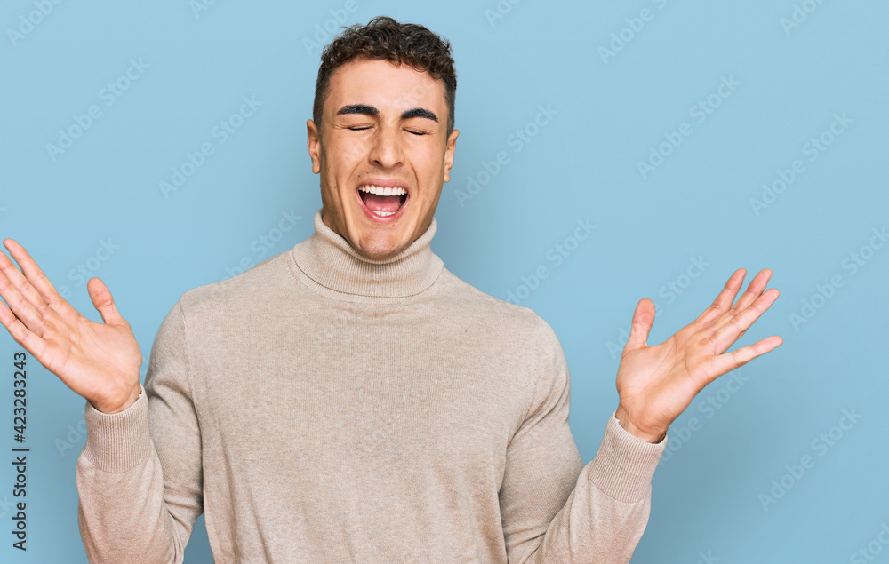 Hispanic young man wearing casual turtleneck sweater celebrating mad and crazy for success with arms raised and closed eyes screaming excited. winner concept Hispanic young man wearing casual turtleneck sweater celebrating mad and crazy for success with arms raised and closed eyes screaming excited. winner concept