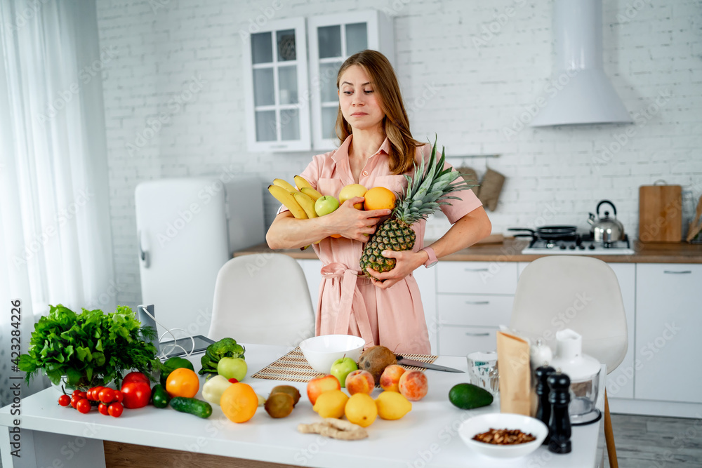 Healthy diet food on the kitchen. Fruits and vegetables laying on table. Pretty woman with healthy food.