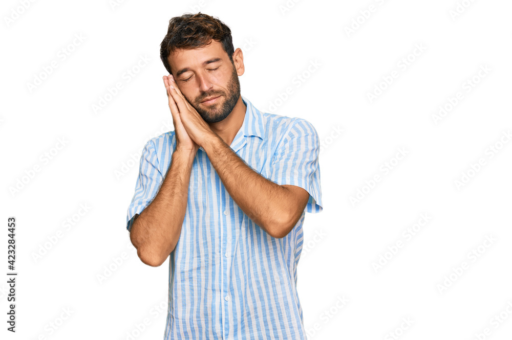 Handsome young man with beard wearing casual fresh shirt sleeping tired dreaming and posing with hands together while smiling with closed eyes. Handsome young man with beard wearing casual fresh shirt sleeping tired dreaming and posing with hands together while smiling with closed eyes.