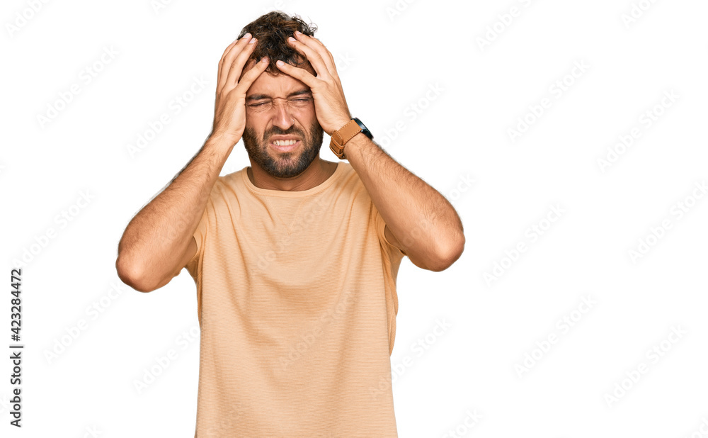 Handsome young man with beard wearing casual tshirt suffering from headache desperate and stressed because pain and migraine. hands on head. Handsome young man with beard wearing casual tshirt suffering from headache desperate and stressed because pain and migraine. hands on head.