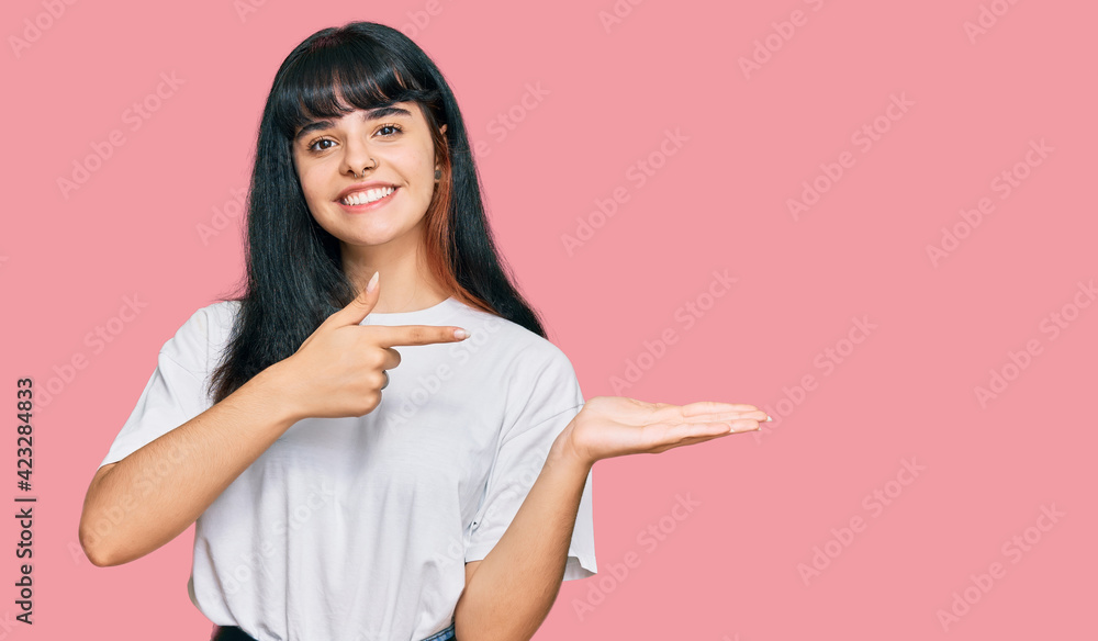 Young hispanic girl wearing casual clothes amazed and smiling to the camera while presenting with hand and pointing with finger. Young hispanic girl wearing casual clothes amazed and smiling to the camera while presenting with hand and pointing with finger.