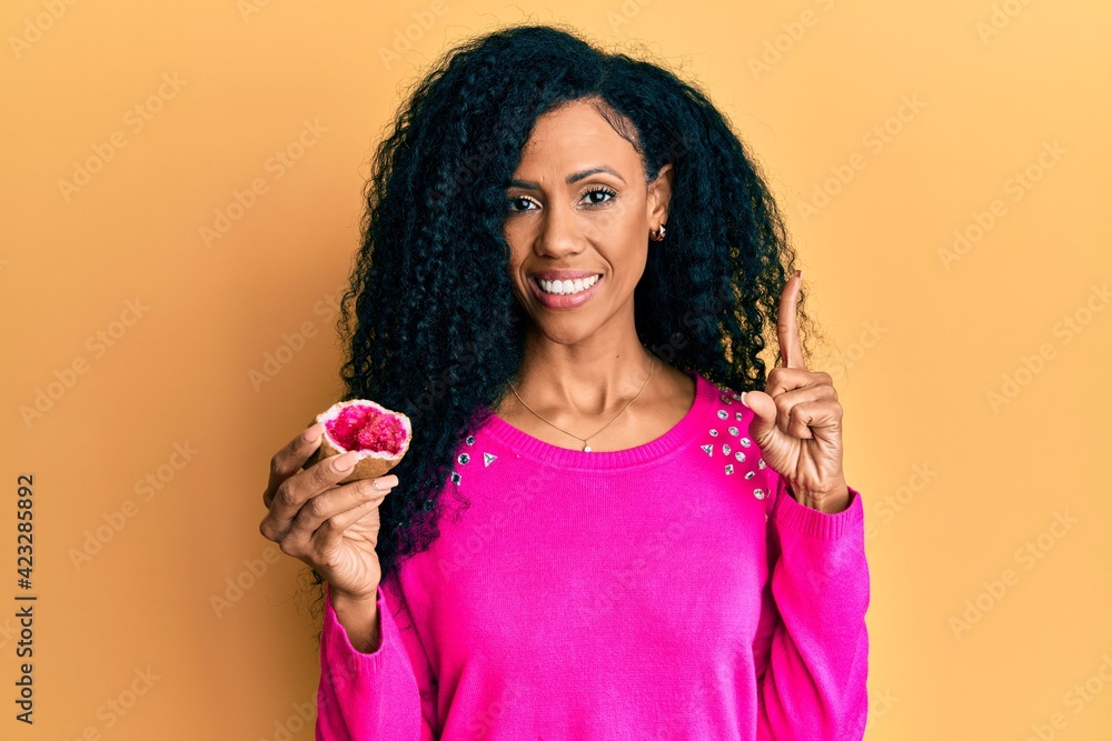 Middle age african american woman holding geode smiling with an idea or question pointing finger with happy face, number one Middle age african american woman holding geode smiling with an idea or question pointing finger with happy face, number one