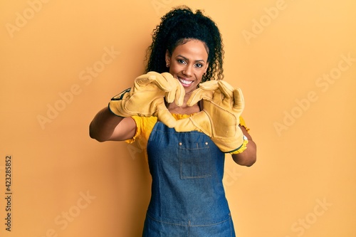Middle age african american woman wearing professional apron smiling in love doing heart symbol shape with hands. romantic concept.