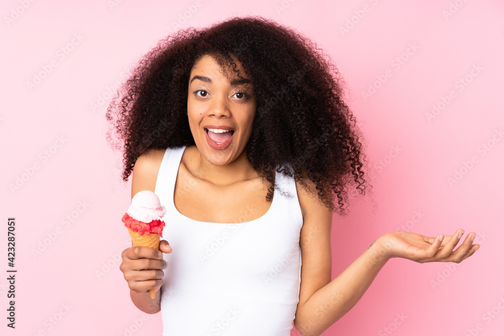 Young african american woman holding a cornet ice cream isolated on pink background with shocked facial expression Young african american woman holding a cornet ice cream isolated on pink background with shocked facial expression