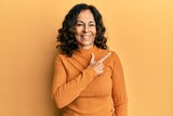 Middle age hispanic woman wearing casual clothes cheerful with a smile of face pointing with hand and finger up to the side with happy and natural expression on face