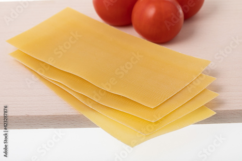 Uncooked lasagna sheets and tomatoes on wooden cutting board