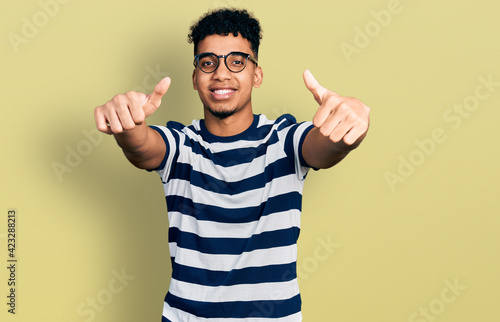 Young african american man wearing casual clothes and glasses approving doing positive gesture with hand  thumbs up smiling and happy for success. winner gesture.