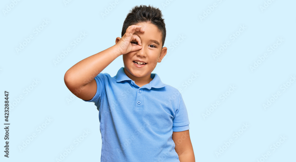 Little boy hispanic kid wearing casual clothes doing ok gesture with hand smiling, eye looking through fingers with happy face. Little boy hispanic kid wearing casual clothes doing ok gesture with hand smiling, eye looking through fingers with happy face.