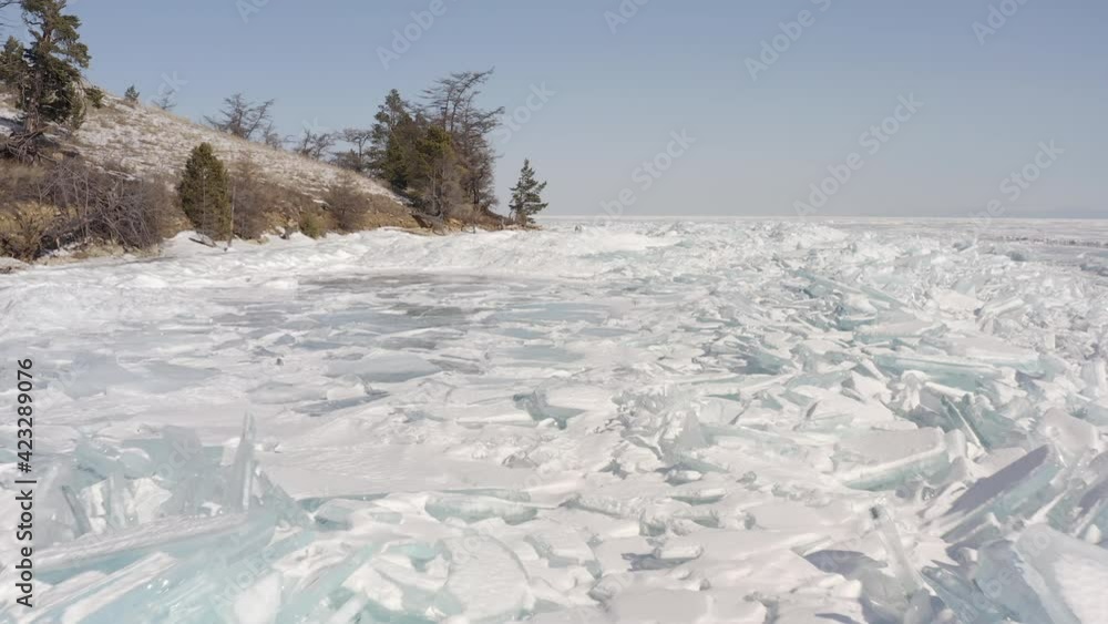 Flight to the right of the hilly shore with trees on Lake Baikal covered with ice and hummocks. Baikal nature Olkhon island Flight to the right of the hilly shore with trees on Lake Baikal covered with ice and hummocks. Baikal nature Olkhon island