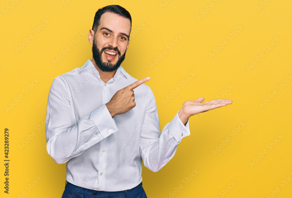 Young man with beard wearing business shirt amazed and smiling to the camera while presenting with hand and pointing with finger. Young man with beard wearing business shirt amazed and smiling to the camera while presenting with hand and pointing with finger.