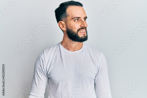 Young man with beard wearing casual white shirt looking to side, relax profile pose with natural face and confident smile.
