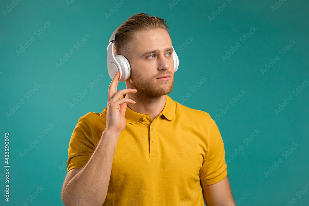 Handsome young man listening to music with wireless headphones, guy having fun, smiling in studio on blue background. Dance, radio concept.