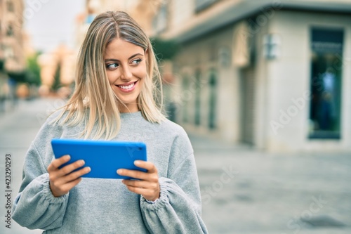 Young blonde girl smiling happy using touchpad at the city.