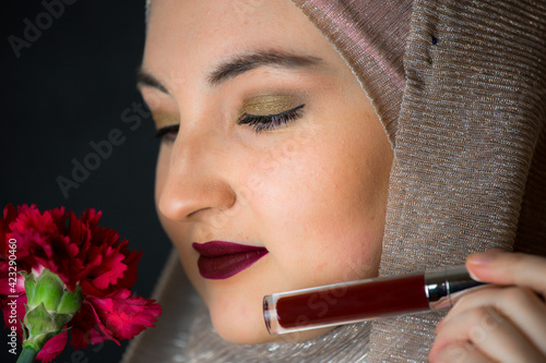 Woman with hijab, professional make-up, showing makeup items, black background, muslim girl