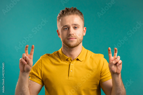 Handsome man showing with hands and two fingers air quotes gesture, bend fingers isolated over blue background. Not funny, irony and sarcasm concept. photo