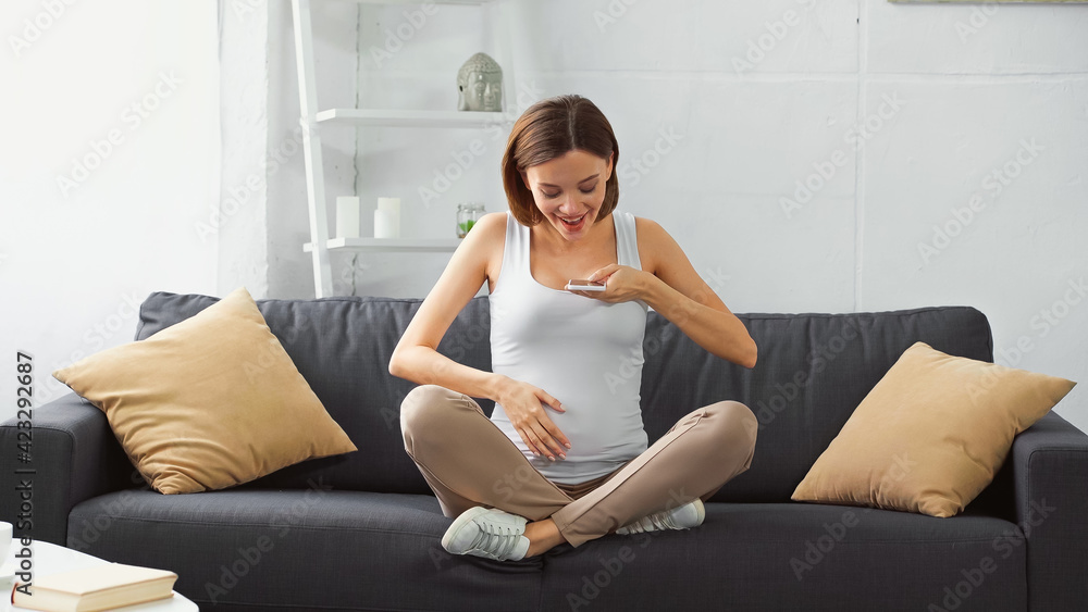 happy pregnant woman touching belly while sending voice message on cellphone happy pregnant woman touching belly while sending voice message on cellphone