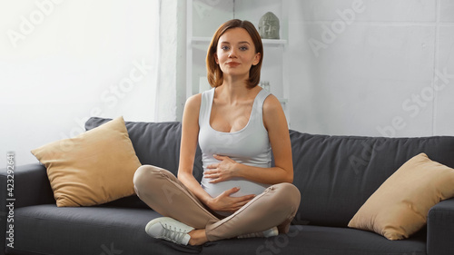 Quadro su tela happy, pregnant woman smiling at camera while sitting on couch with crossed legs