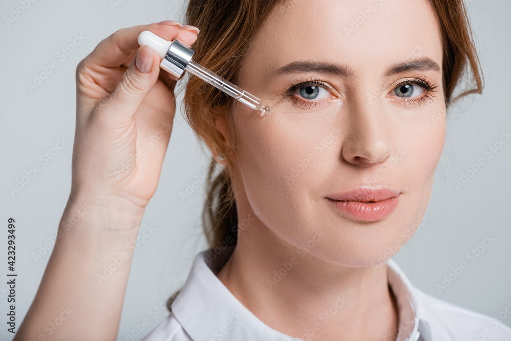 Female hand holding cosmetic serum near face of woman isolated on grey Female hand holding cosmetic serum near face of woman isolated on grey