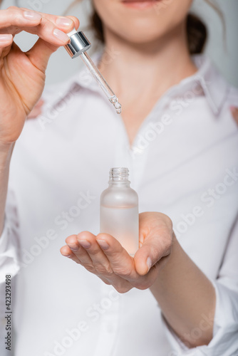 Cropped view of woman on blurred background holding cosmetic serum isolated on grey