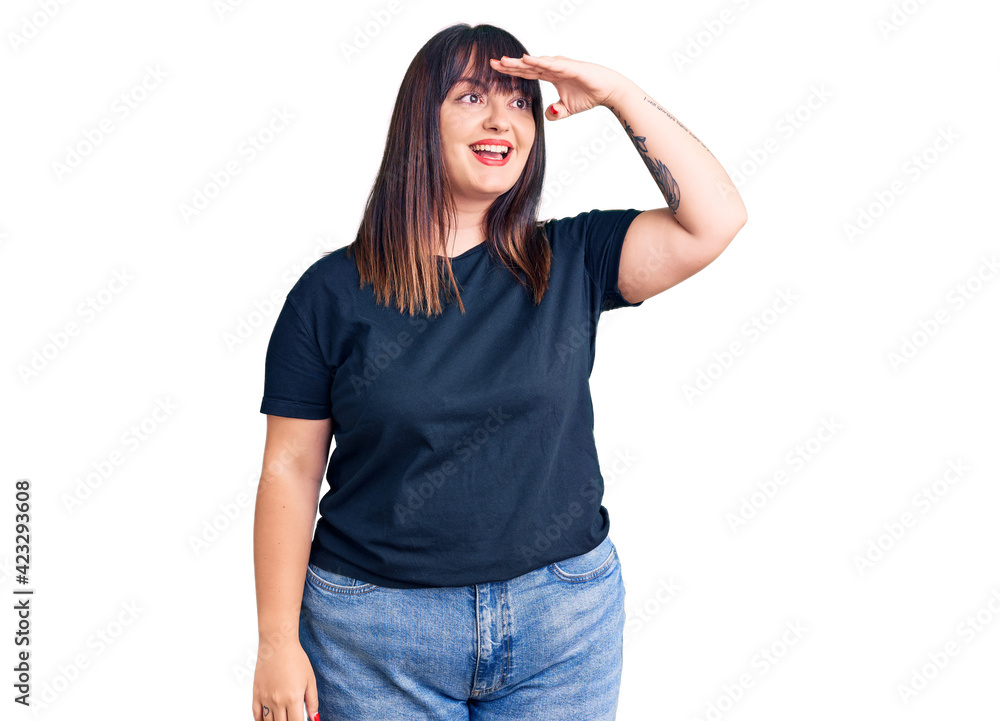 Young plus size woman wearing casual clothes very happy and smiling looking far away with hand over head. searching concept. Young plus size woman wearing casual clothes very happy and smiling looking far away with hand over head. searching concept.