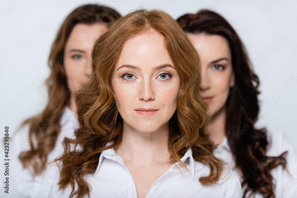 Red haired woman looking at camera near friends blurred on background isolated on grey Red haired woman looking at camera near friends blurred on background isolated on grey