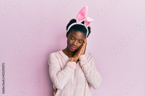 Young african american girl wearing cute easter bunny ears sleeping tired dreaming and posing with hands together while smiling with closed eyes.