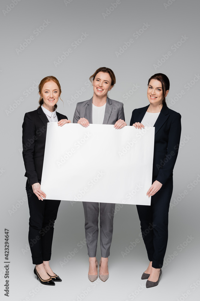 Cheerful businesswomen with white placard on grey background Cheerful businesswomen with white placard on grey background
