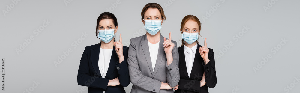 Businesswomen in medical masks pointing with fingers isolated on grey, banner Businesswomen in medical masks pointing with fingers isolated on grey, banner
