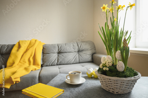 Spring Easter home interior in living room with coffee, pled. flowers and notebook in trendy colors grey and yellow. Domestic life.