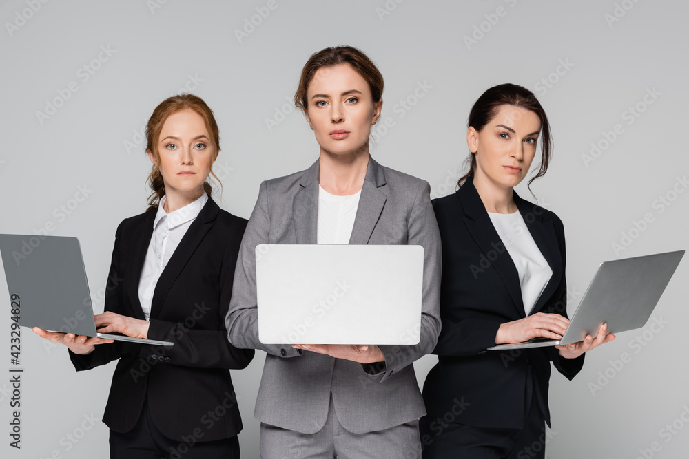 Adult businesswomen with laptops looking at camera isolated on grey Adult businesswomen with laptops looking at camera isolated on grey