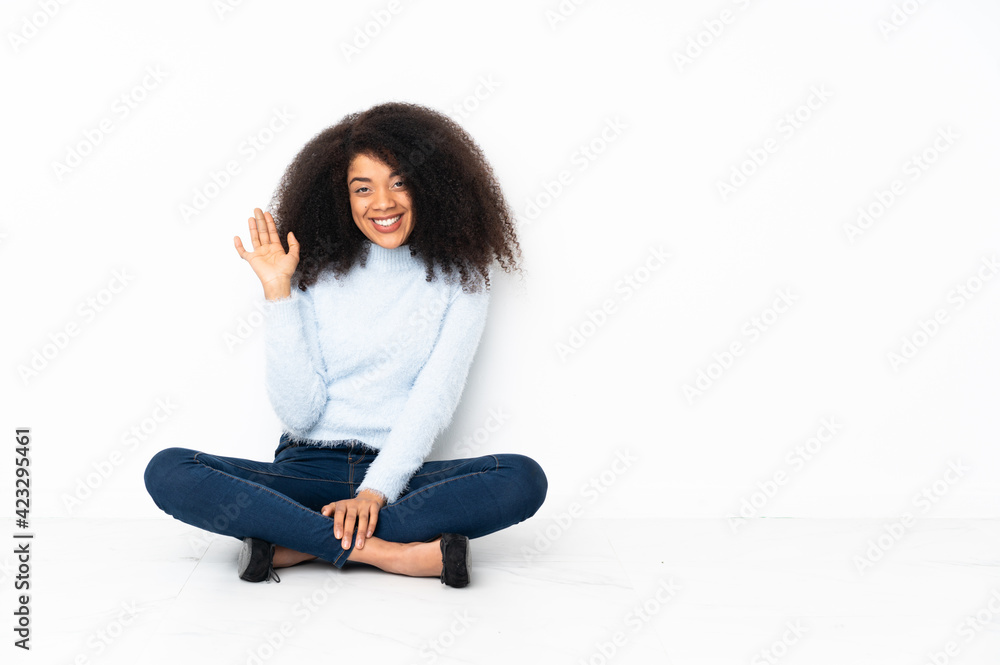 Young african american woman sitting on the floor saluting with hand with happy expression