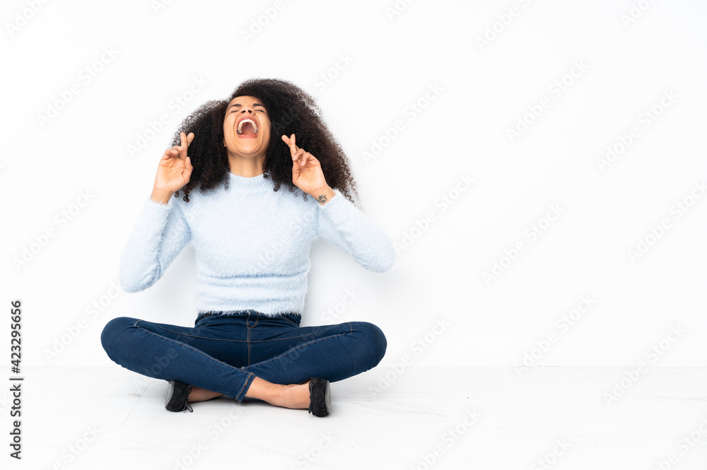 Young african american woman sitting on the floor with fingers crossing Young african american woman sitting on the floor with fingers crossing