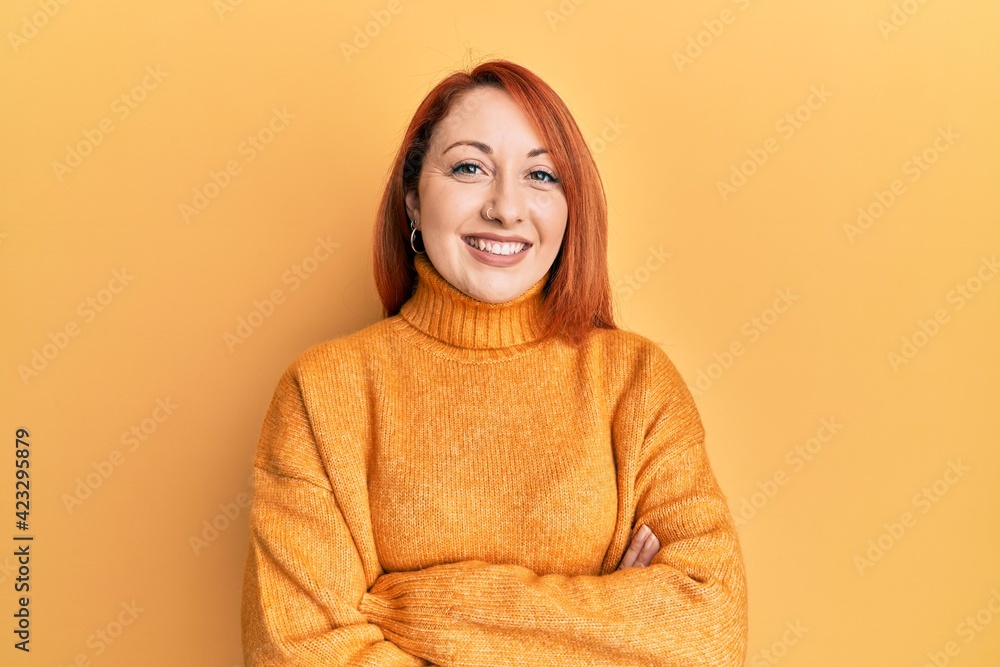 Beautiful redhead woman wearing casual winter sweater over yellow background happy face smiling with crossed arms looking at the camera. positive person. Beautiful redhead woman wearing casual winter sweater over yellow background happy face smiling with crossed arms looking at the camera. positive person.