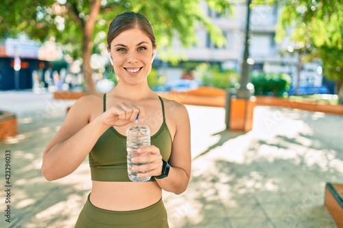 Young blonde sportswoman doing exercise drinking bottle of water at the city.