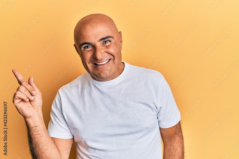 Mature middle east man wearing casual white tshirt with a big smile on face, pointing with hand and finger to the side looking at the camera. Mature middle east man wearing casual white tshirt with a big smile on face, pointing with hand and finger to the side looking at the camera.