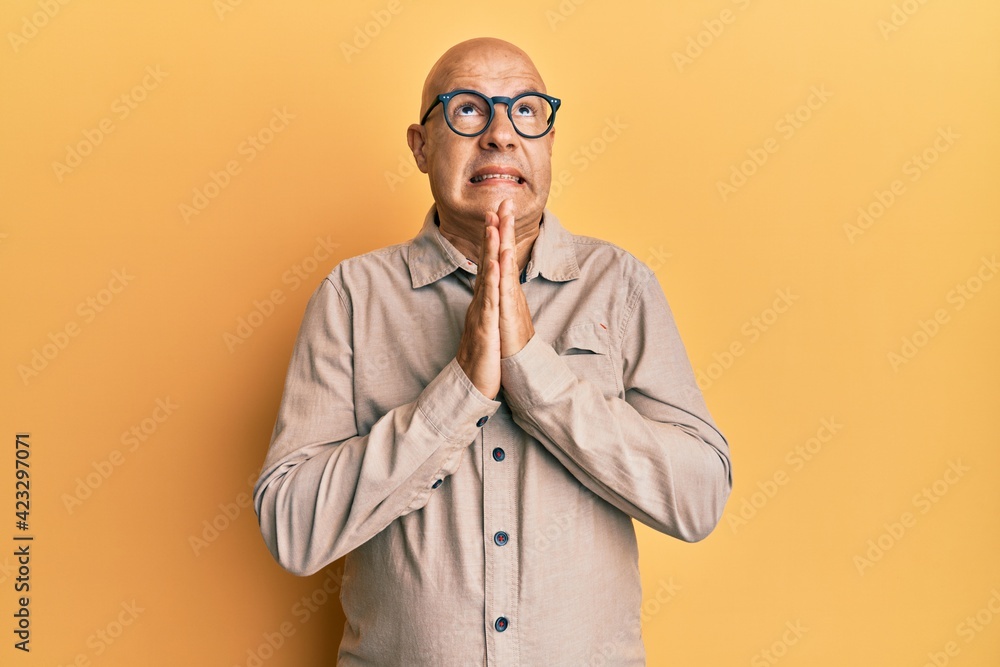 Middle age bald man wearing casual clothes and glasses begging and praying with hands together with hope expression on face very emotional and worried. begging. Middle age bald man wearing casual clothes and glasses begging and praying with hands together with hope expression on face very emotional and worried. begging.