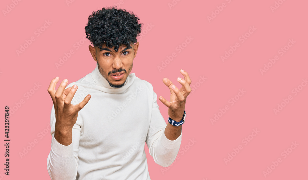Young arab man wearing casual winter sweater shouting frustrated with rage, hands trying to strangle, yelling mad Young arab man wearing casual winter sweater shouting frustrated with rage, hands trying to strangle, yelling mad
